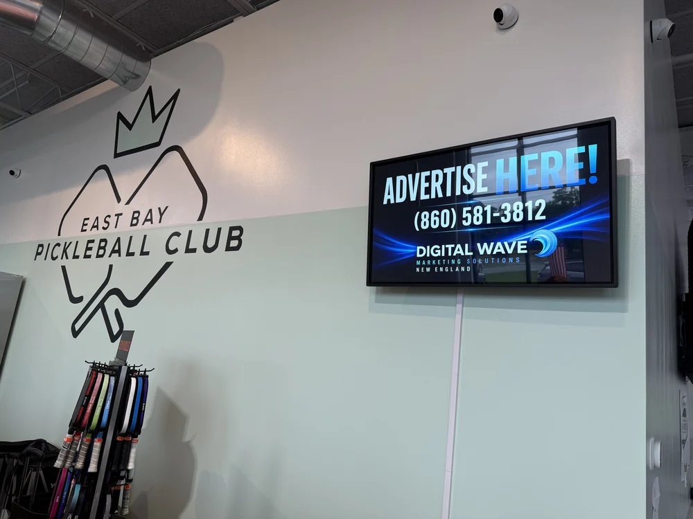 Wall-mounted Digital Wave screen at East Bay Pickleball Club in Warren, Rhode Island, beside the club&rsquo;s own logo
